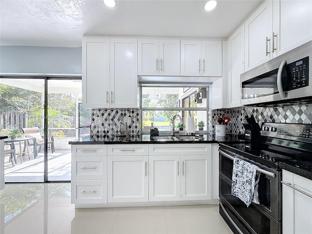 kitchen featuring sink, stainless steel appliances, light tile patterned floors, decorative backsplash, and white cabinets