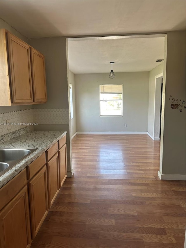 kitchen with backsplash, dark hardwood / wood-style floors, light stone counters, and hanging light fixtures