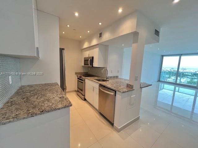 kitchen with light stone countertops, stainless steel appliances, floor to ceiling windows, and white cabinets