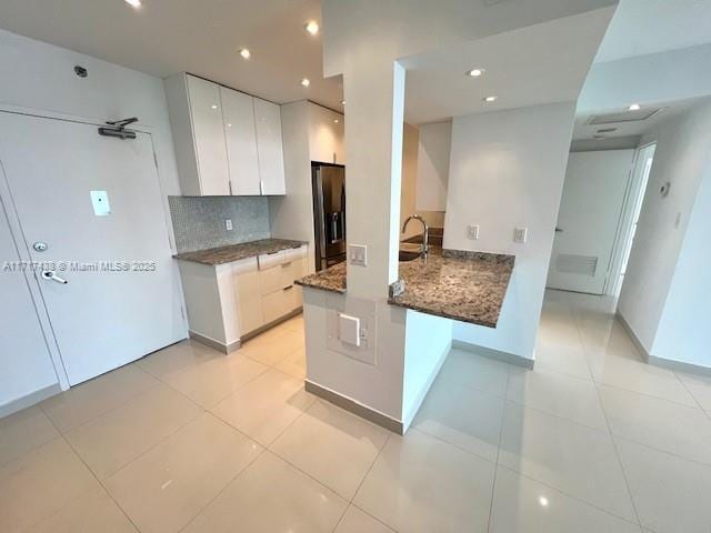 kitchen featuring white cabinetry, stainless steel fridge with ice dispenser, light tile patterned floors, kitchen peninsula, and decorative backsplash