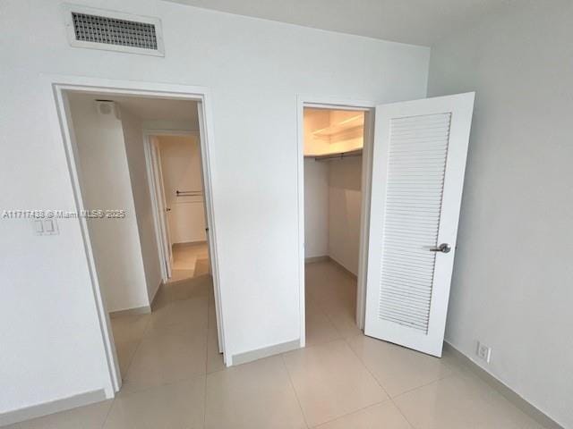 unfurnished bedroom featuring a walk in closet, light tile patterned floors, and a closet