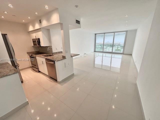 kitchen featuring sink, appliances with stainless steel finishes, expansive windows, dark stone counters, and white cabinets