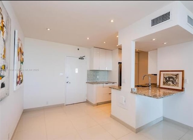 kitchen with white cabinetry, light tile patterned floors, kitchen peninsula, light stone countertops, and backsplash