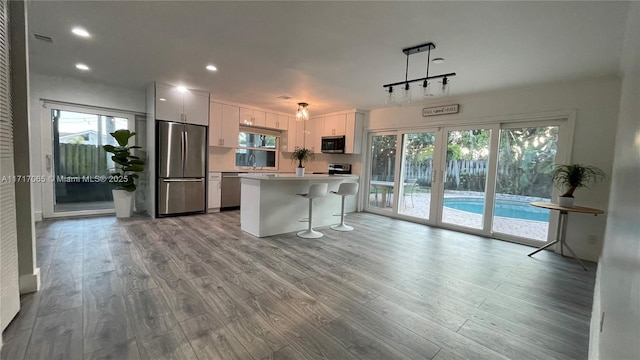 kitchen with a kitchen breakfast bar, stainless steel appliances, pendant lighting, white cabinets, and a kitchen island