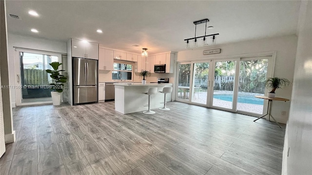 kitchen with hanging light fixtures, stainless steel appliances, a kitchen island, a kitchen breakfast bar, and white cabinets