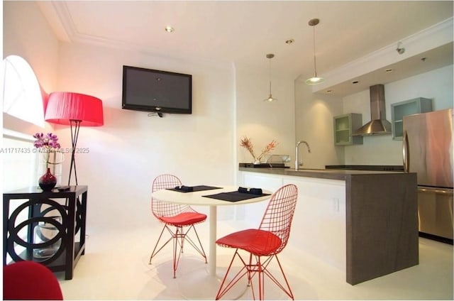 kitchen with sink, stainless steel refrigerator, ornamental molding, white cabinets, and wall chimney exhaust hood