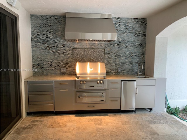 kitchen with gray cabinetry, refrigerator, wall chimney range hood, sink, and tasteful backsplash