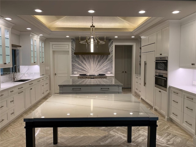 kitchen with a raised ceiling, white cabinetry, sink, and ornamental molding