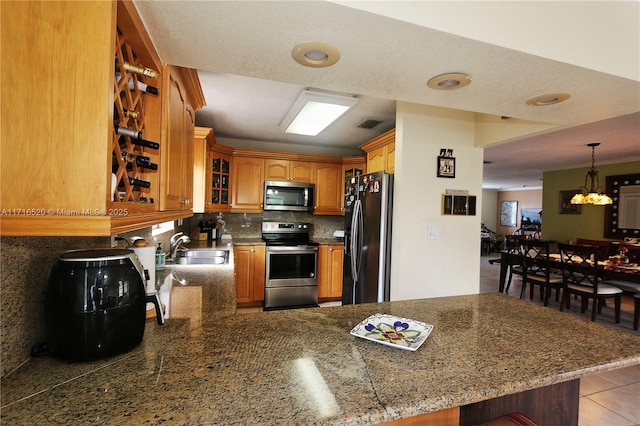 kitchen with sink, stainless steel appliances, an inviting chandelier, backsplash, and kitchen peninsula