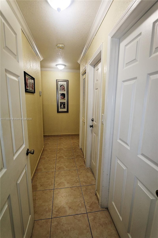 hall with a textured ceiling, ornamental molding, and light tile patterned flooring