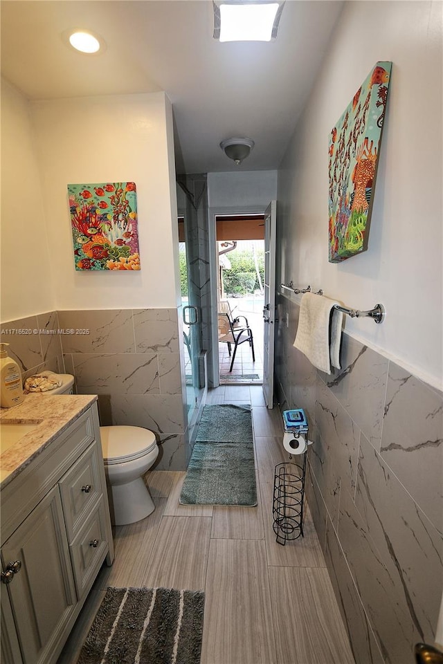 bathroom featuring walk in shower, vanity, toilet, and tile walls