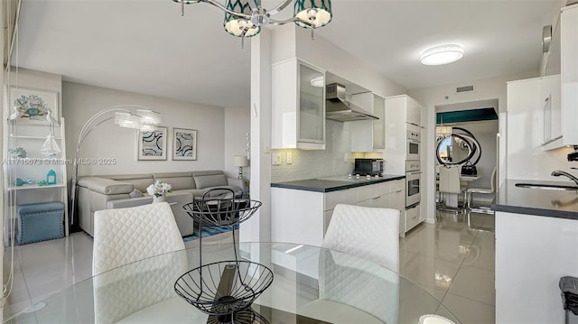 kitchen featuring decorative backsplash, sink, wall chimney range hood, a notable chandelier, and white cabinetry