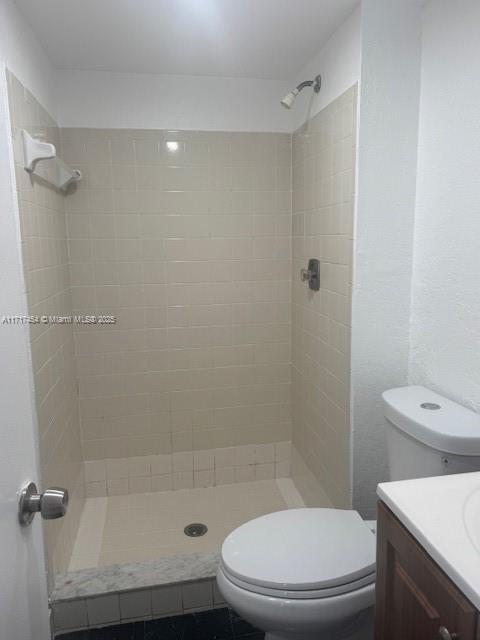 bathroom with a tile shower, vanity, and toilet