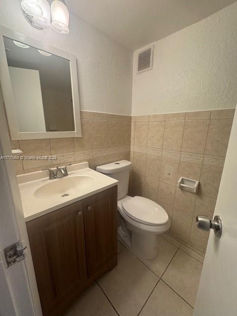 bathroom featuring tile patterned floors, vanity, toilet, and tile walls