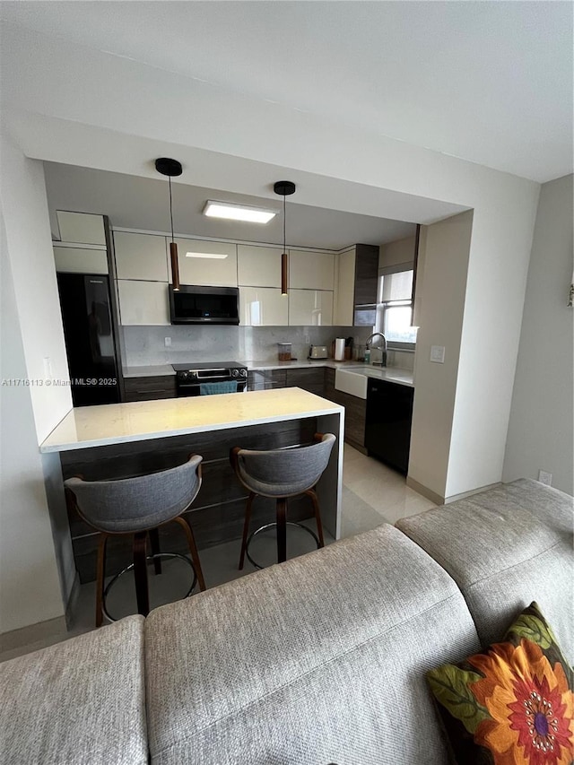 kitchen featuring pendant lighting, black appliances, decorative backsplash, a kitchen bar, and kitchen peninsula