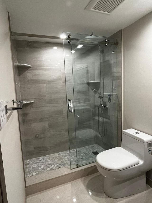 bathroom featuring tile patterned flooring, toilet, and a shower with door