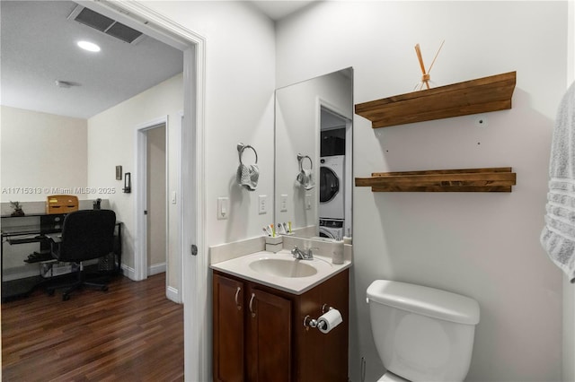 bathroom with vanity, stacked washing maching and dryer, toilet, and hardwood / wood-style flooring