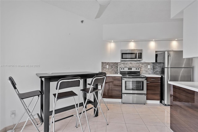 kitchen with light tile patterned floors, backsplash, stainless steel appliances, and dark brown cabinetry