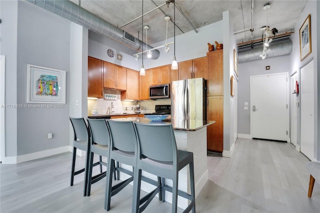 kitchen featuring hanging light fixtures, light hardwood / wood-style flooring, stainless steel appliances, and a high ceiling