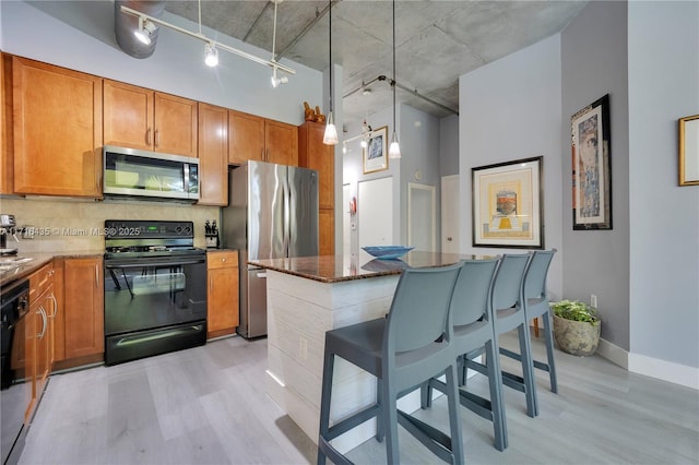 kitchen with a breakfast bar, pendant lighting, dark stone counters, a high ceiling, and black appliances