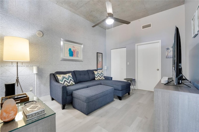 living room featuring a high ceiling, ceiling fan, and light wood-type flooring