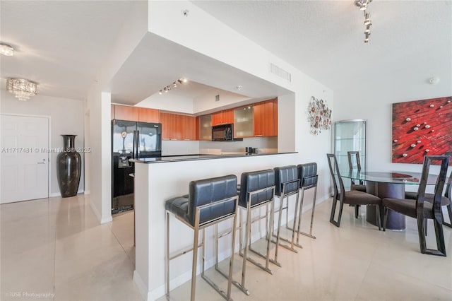 kitchen featuring kitchen peninsula, a breakfast bar, a textured ceiling, black appliances, and light tile patterned floors