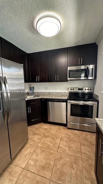 kitchen featuring light stone countertops, a textured ceiling, stainless steel appliances, and dark brown cabinetry