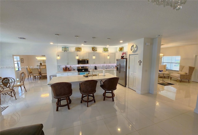 kitchen with appliances with stainless steel finishes, backsplash, a breakfast bar, white cabinets, and hanging light fixtures