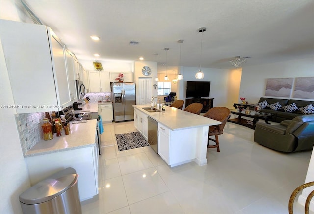 kitchen featuring a center island with sink, sink, appliances with stainless steel finishes, decorative light fixtures, and white cabinetry