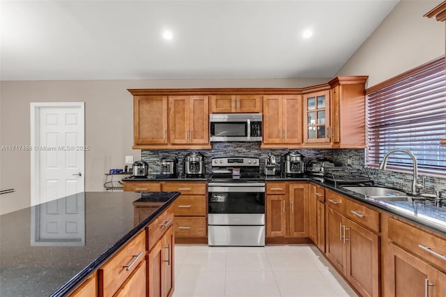 kitchen featuring backsplash, dark stone counters, sink, light tile patterned flooring, and stainless steel appliances