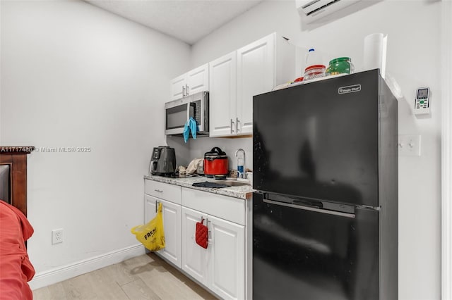 kitchen featuring white cabinets, light hardwood / wood-style floors, black fridge, and sink