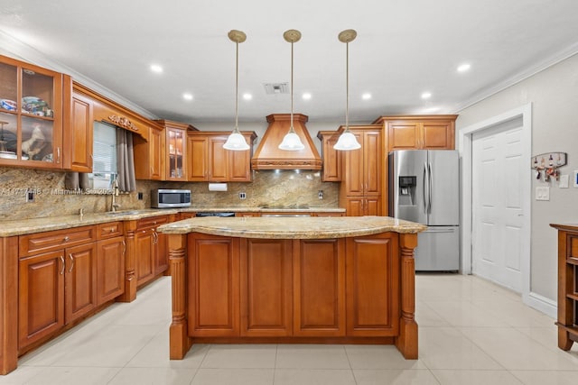 kitchen with appliances with stainless steel finishes, premium range hood, ornamental molding, decorative light fixtures, and a kitchen island