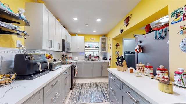 kitchen with gray cabinetry, sink, decorative backsplash, light stone countertops, and appliances with stainless steel finishes