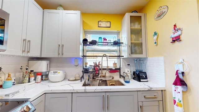 kitchen featuring decorative backsplash, light stone counters, range, and sink