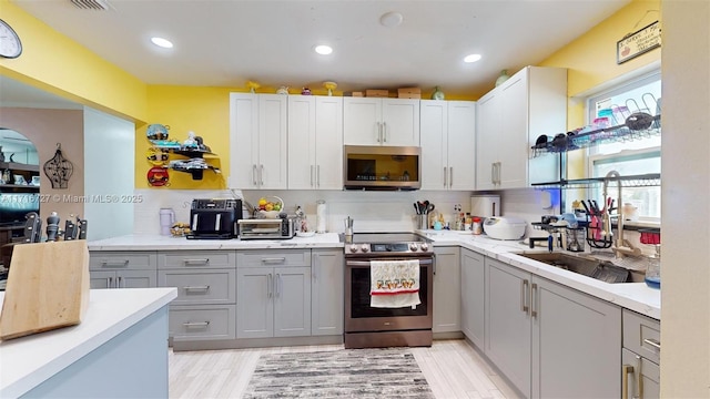 kitchen with stainless steel appliances, gray cabinets, tasteful backsplash, and light hardwood / wood-style flooring