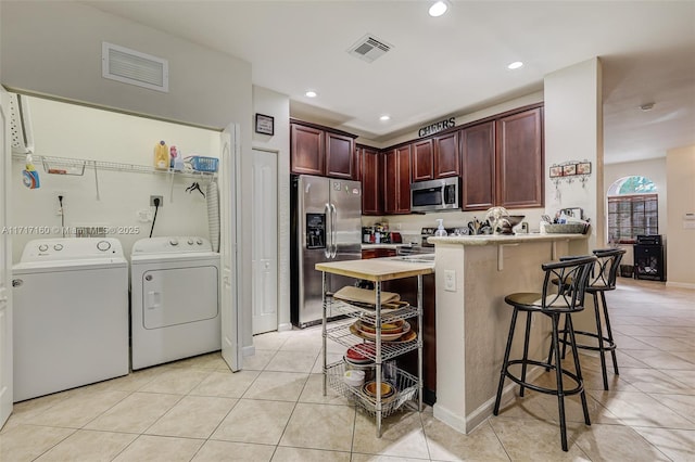 kitchen with a kitchen breakfast bar, washer and clothes dryer, light tile patterned flooring, and stainless steel appliances