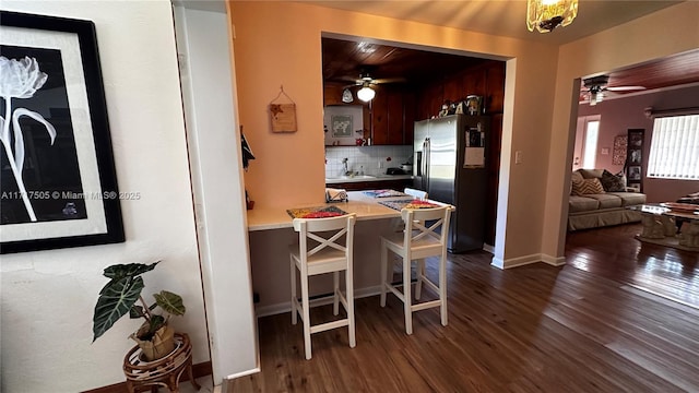 kitchen featuring decorative backsplash, stainless steel fridge, dark hardwood / wood-style flooring, a breakfast bar, and ceiling fan