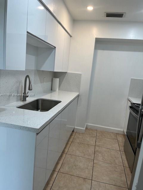 kitchen featuring black range with electric stovetop, sink, light stone counters, light tile patterned flooring, and white cabinets