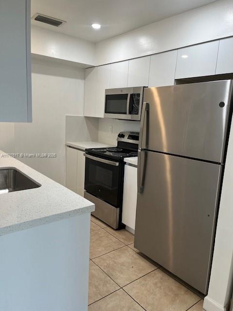 kitchen featuring appliances with stainless steel finishes, light stone counters, sink, light tile patterned floors, and white cabinetry