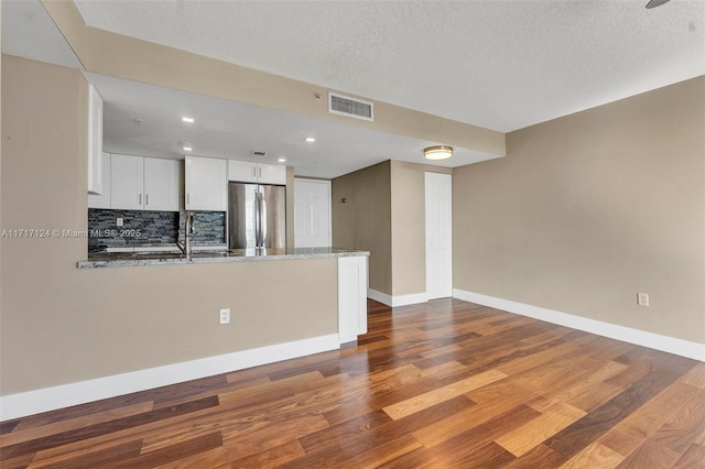 kitchen with visible vents, stainless steel refrigerator, dark wood-style flooring, a peninsula, and white cabinetry