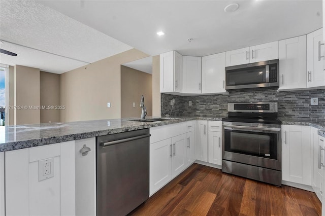 kitchen with stone countertops, appliances with stainless steel finishes, dark wood-type flooring, a sink, and backsplash