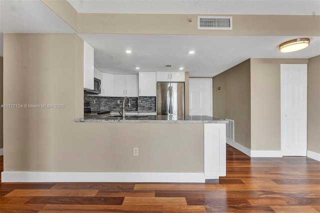 kitchen featuring stone countertops, visible vents, appliances with stainless steel finishes, a peninsula, and a sink