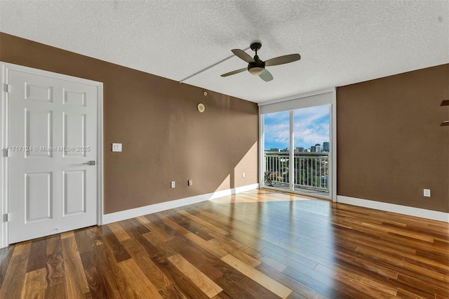 empty room featuring a textured ceiling, a wall of windows, wood finished floors, and baseboards