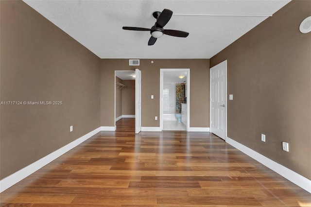 unfurnished bedroom with ensuite bathroom, wood finished floors, visible vents, baseboards, and a walk in closet