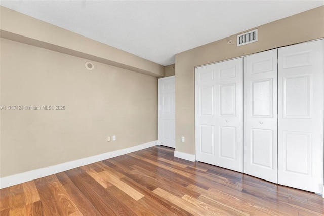 unfurnished bedroom featuring a closet, visible vents, baseboards, and wood finished floors