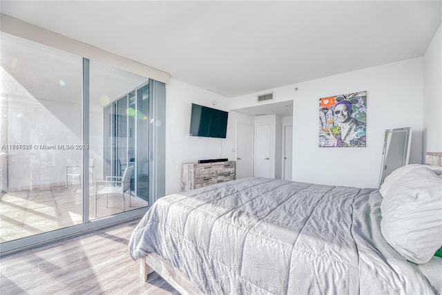 bedroom with multiple windows, hardwood / wood-style floors, expansive windows, and access to exterior