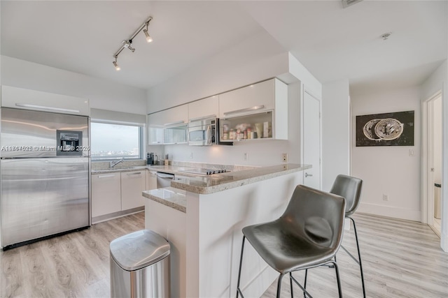 kitchen with a kitchen breakfast bar, kitchen peninsula, light hardwood / wood-style flooring, appliances with stainless steel finishes, and white cabinetry