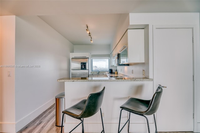 kitchen featuring light stone countertops, stainless steel fridge, and white cabinetry