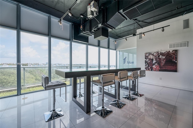 tiled dining space featuring floor to ceiling windows, rail lighting, and a high ceiling