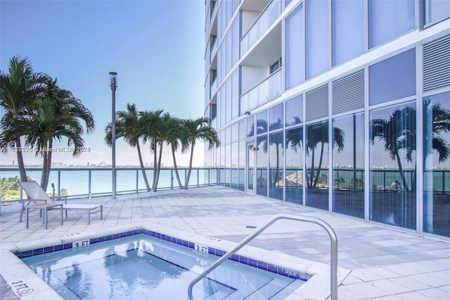 pool at dusk featuring a water view, a patio, and a hot tub